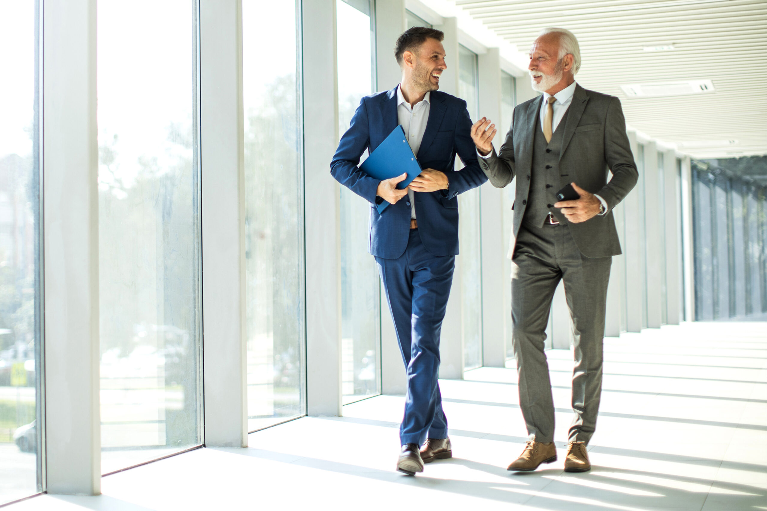 Senior and junior management business people walking through hallway and talking