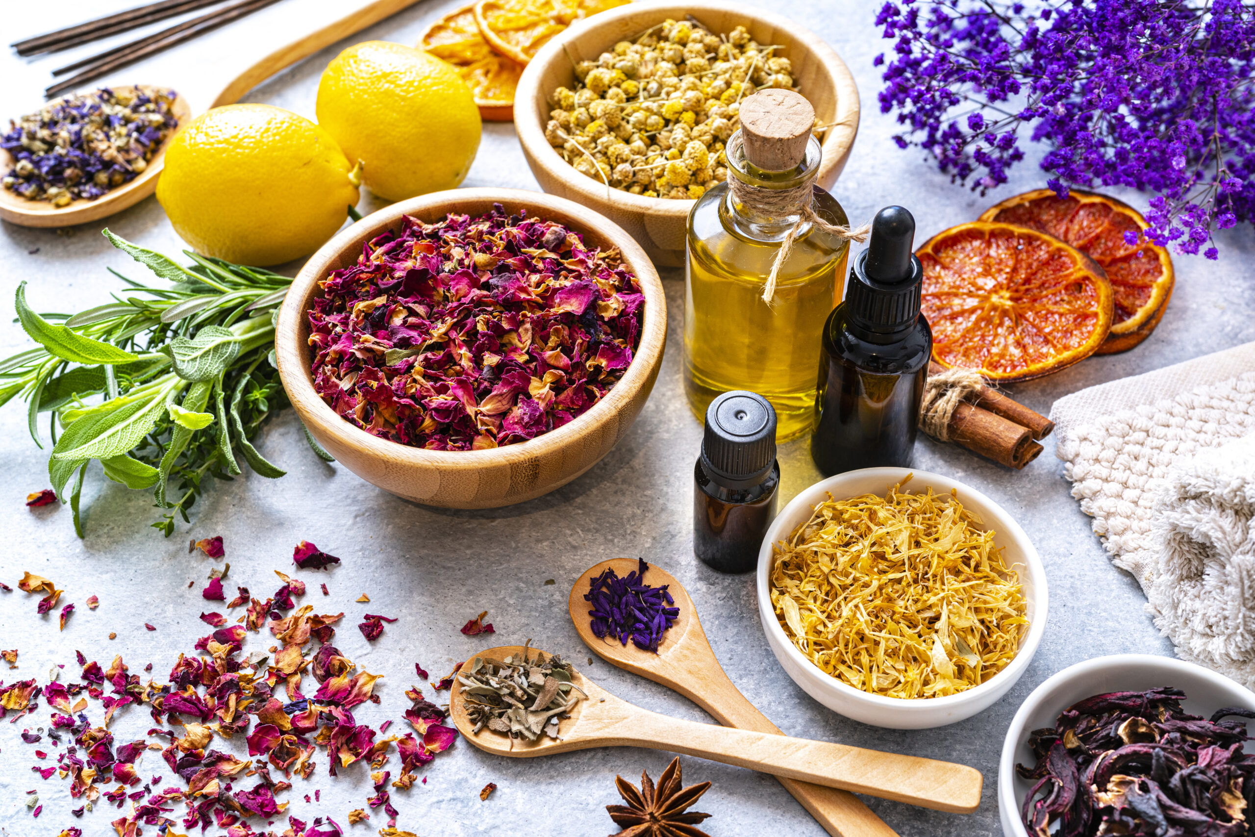 group of dried herbal tea leaves, flower petals, essential oils, massage oils, dried orange slices, cinnamon sticks, star anise, herbs, and incense sticks arranged on a table
